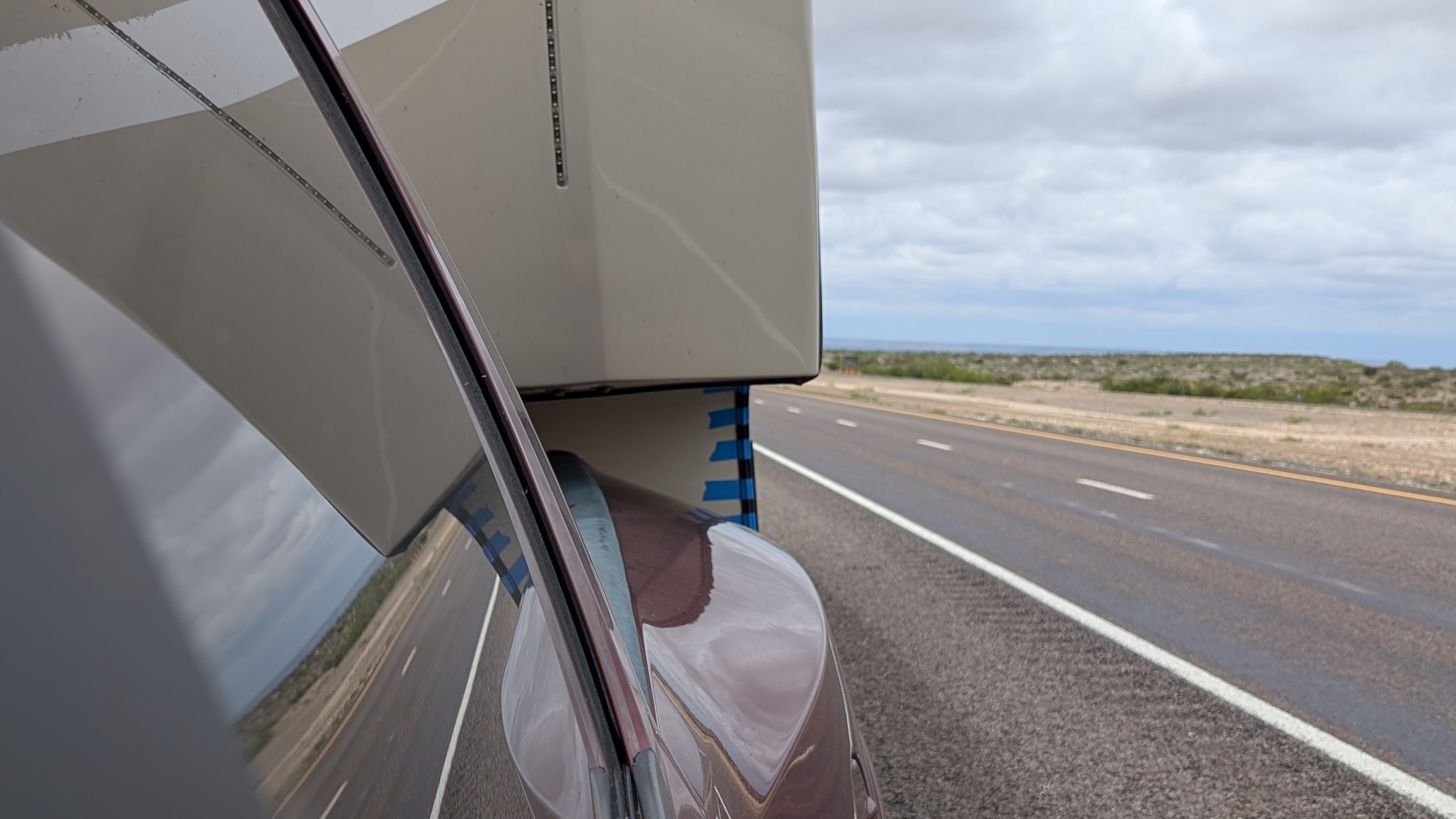 Driver's view of a fifth wheel connected to a truck showing strips of blue tape over trim